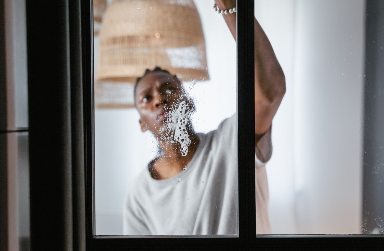 An adult male cleaning a glass window indoors, focusing on household chores and cleanliness.